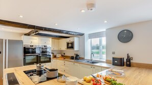 Een moderne keuken met roestvrijstalen apparatuur, een groot eiland met vers fruit en groenten, en een uitzicht op de omgeving door een raam.