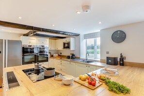 A modern kitchen with stainless steel appliances, a large island with fresh produce, and a view of the outdoors through a window.