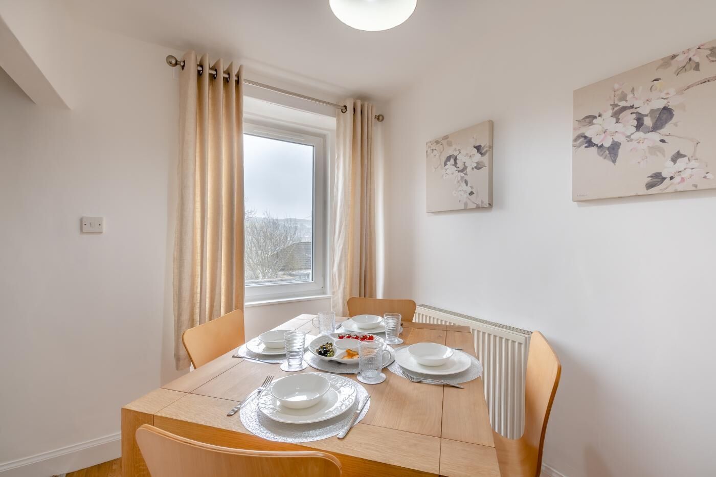 Een eetgedeelte met een tafel voor vier personen, een raam met gordijnen en een radiator.
