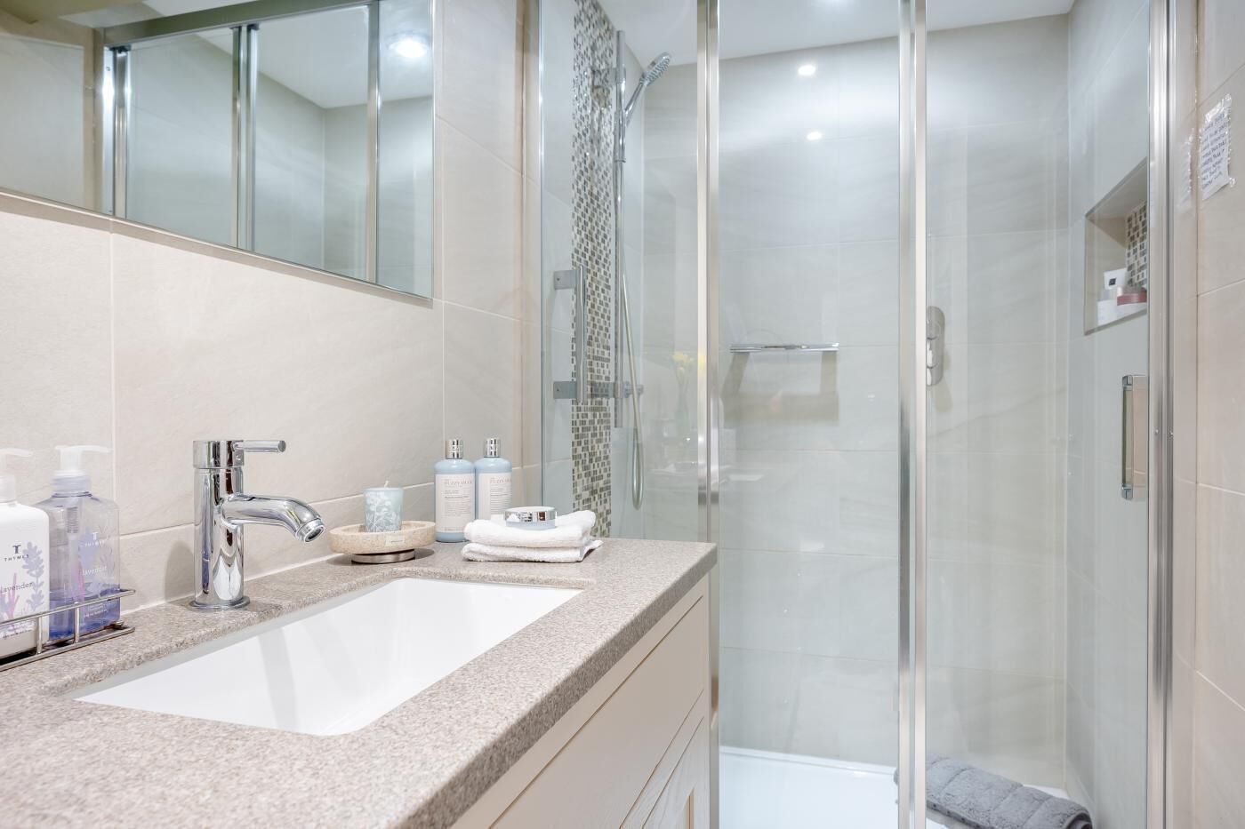 A modern bathroom with a glass-enclosed shower, a sink with a mirror above, and toiletries on the counter.