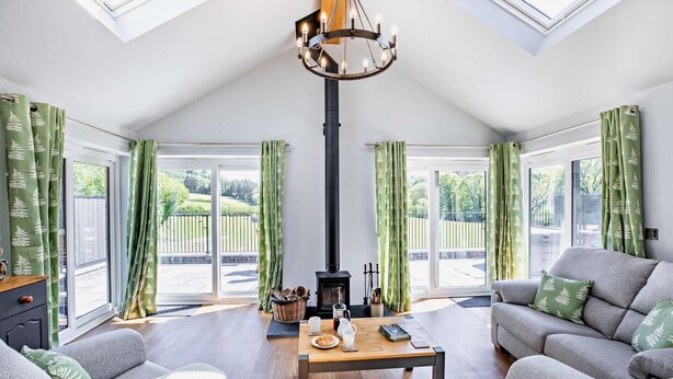 A spacious living room with a fireplace, two sofas, a coffee table, and a chandelier. - 2 Bed in Llanarmon Dyffryn Ceiriog (oc-b31110) (Llanarmon Dyffryn Ceiriog)