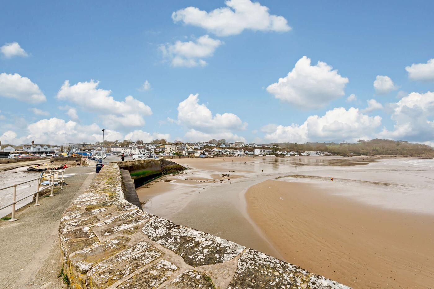 A coastal town with a sandy beach, stone walls, and a clear sky.