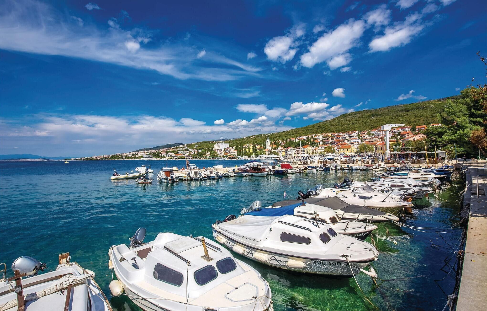Un port de plaisance où sont amarrés plusieurs bateaux, un ciel bleu dégagé et une ville en arrière-plan.