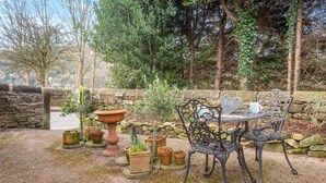 A garden patio with a stone wall, potted plants, a metal table and chairs, and a heart-shaped sign. - 1 Bed in Starkholmes (oc-q30994) (Matlock Bath)