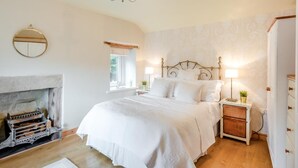 A bedroom with a fireplace, a bed with white bedding, a nightstand with a lamp, and a wall-mounted mirror. - 1 Bed in Starkholmes (oc-q30994) (Matlock Bath)
