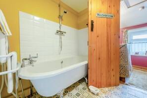 Un baño con una bañera blanca, ducha, una puerta de madera con la leyenda 'WASHROOM' y una ventana con cortinas.