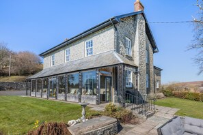 A stone house with a glass conservatory, a stone staircase, and a lawn. - 5 Bed in Hundred House (oc-l31090) (Hundred House)