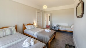 Ein Zimmer mit zwei Einzelbetten, einem Holzkopfteil, einem Nachttisch mit Lampe, einem Spiegel an der Wand und einer Tür zu einem anderen Raum.
