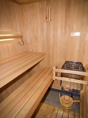 Een sauna met houten banken, een stoomgenerator en een houten emmer.