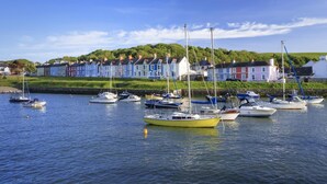 A harbor with multiple boats docked, a row of colorful houses in the background, and a grassy area with trees. - 5 Bed in Ystrad Meurig (oc-r31133) (Ystrad Meurig)