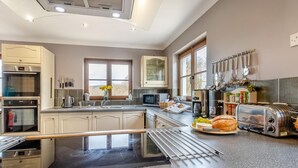 A modern kitchen with a central island, stainless steel appliances, and a variety of utensils on the wall. - 5 Bed in Ystrad Meurig (oc-r31133) (Ystrad Meurig)