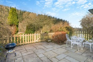 A patio with a barbecue grill, white metal chairs, and a wooden fence. - 2 Bed in Pooley Bridge (oc-l31060) (Pooley Bridge)