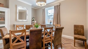 A dining area with a wooden table, chairs, a chandelier, and a large mirror.