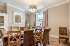 Un espace repas comprenant une table en bois, des chaises, un lustre et un grand miroir.