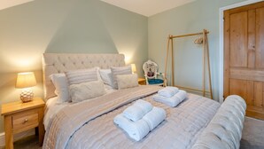 A bedroom with a tufted headboard, a wooden side table with a lamp, a chair with a cushion, and a wooden wardrobe.