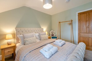 Une chambre à coucher avec une tête de lit capitonnée, une table de chevet en bois avec une lampe, une chaise avec un coussin et une armoire en bois.