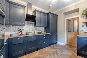 Une cuisine moderne avec des meubles de couleur sombre, un parquet en bois disposé en chevrons et un dosseret carrelé.