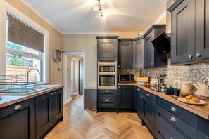 A modern kitchen with dark cabinetry, a built-in oven, microwave, and a window with a view of the outside. - 6 Bed in Buxton (oc-s31063) (Buxton)