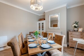 Une salle à manger avec une table en bois dressée pour six personnes, un lustre, un miroir et une commode à tiroirs.