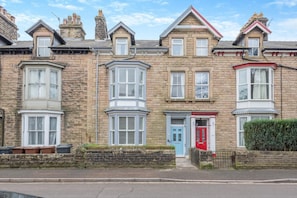 Une rangée de maisons mitoyennes avec des bow-windows, une porte rouge et une façade en pierre.