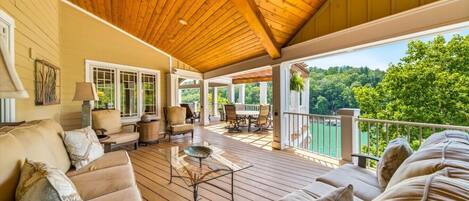 A covered deck with wooden flooring, outdoor furniture, and a view of a lake.