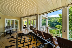 A covered outdoor area with a foosball table, seating, and a view of a green landscape. - Lux Norris Lake Home|Private Dock & Stunning Views (LaFollette)