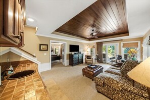 A spacious living room with a large sofa, a television, and a ceiling fan. - Lux Norris Lake Home|Private Dock & Stunning Views (LaFollette)