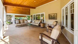 Eine überdachte Veranda mit Holzboden, einer Sofagarnitur, einem Couchtisch und einem Sessel.