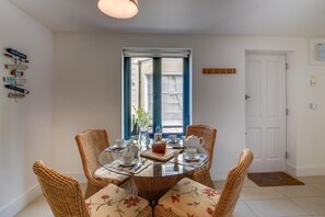 A dining area with wicker chairs and a glass table, a window with blue shutters, and wall-mounted signs. - 2 Bed in Torquay (oc-wellme) (Torquay)