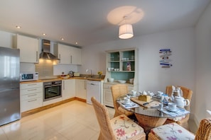 A modern kitchen with white cabinets, stainless steel appliances, and a dining area with wicker chairs and a glass table. - 2 Bed in Torquay (oc-wellme) (Torquay)