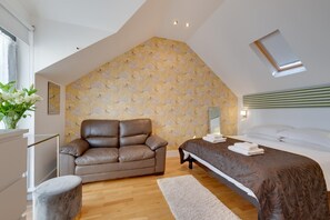 A bedroom with a sloped ceiling, a brown leather sofa, a bed with a dark patterned bedspread, and a floral wallpaper. - 2 Bed in Torquay (oc-wellme) (Torquay)