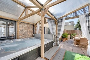 A hot tub area with stone walls, wooden beams, and a covered patio with outdoor furniture. - 2 Bed in Torquay (oc-wellme) (Torquay)