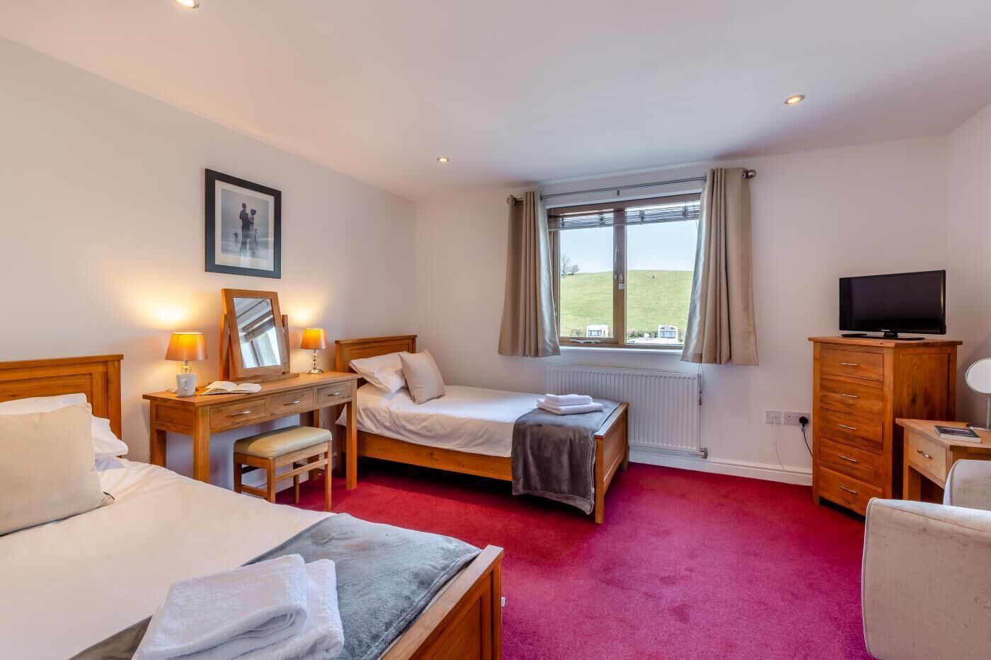 Quarto de hotel com duas camas, uma escrivaninha, uma cadeira, uma televisão e uma janela com cortinas.