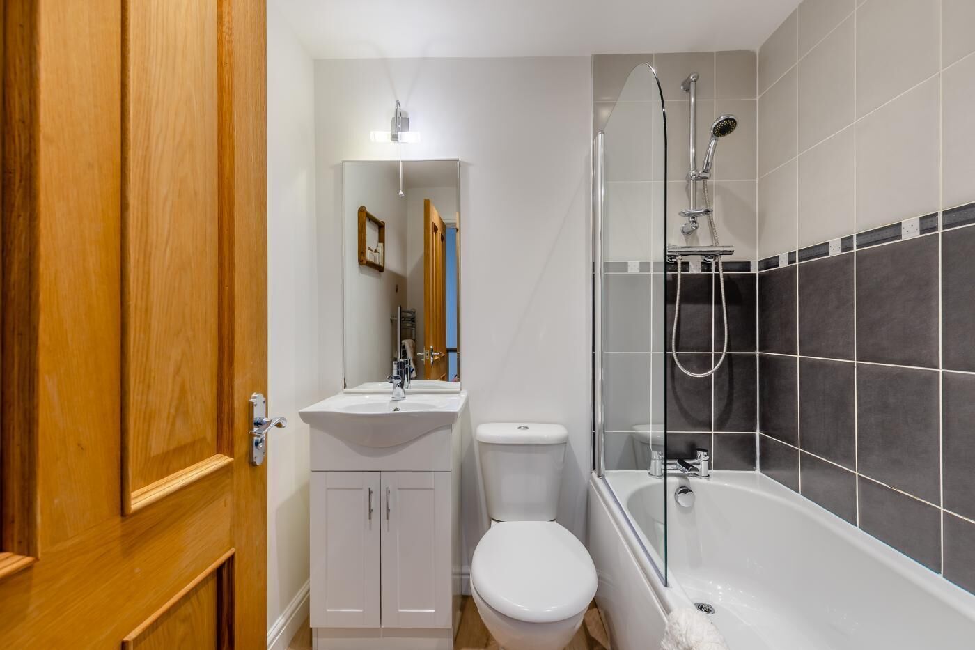 A bathroom with a white sink, toilet, and bathtub, wooden door, and tiled walls.