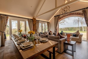 Een eethoek met een lange tafel gedekt voor een maaltijd, een zithoek en uitzicht op het groen.