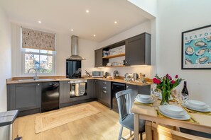 A modern kitchen with dark cabinetry, a built-in oven, a microwave, and a dining area with a table set for two. - 2 Bed in Scarborough (oc-f31046) (Scarborough)