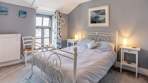 Een slaapkamer met een bed, twee nachtkastjes, een stoel, een radiator en een raam met gordijnen.