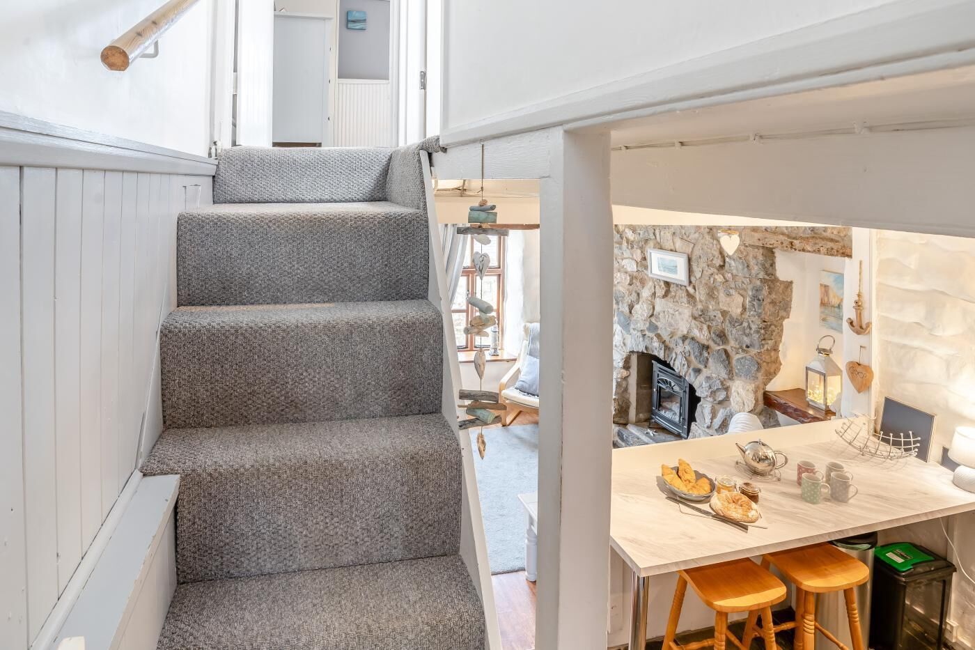 Un escalier mène à une salle à manger agrémentée d’un mur en pierre, d’une cheminée et d’une table mise.