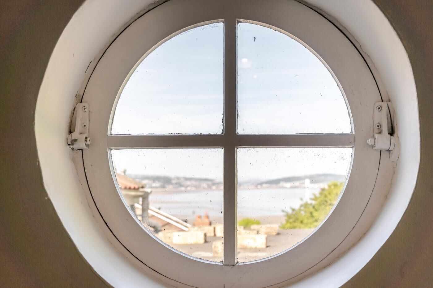 A round window with four panes, offering a view of a body of water and distant buildings.