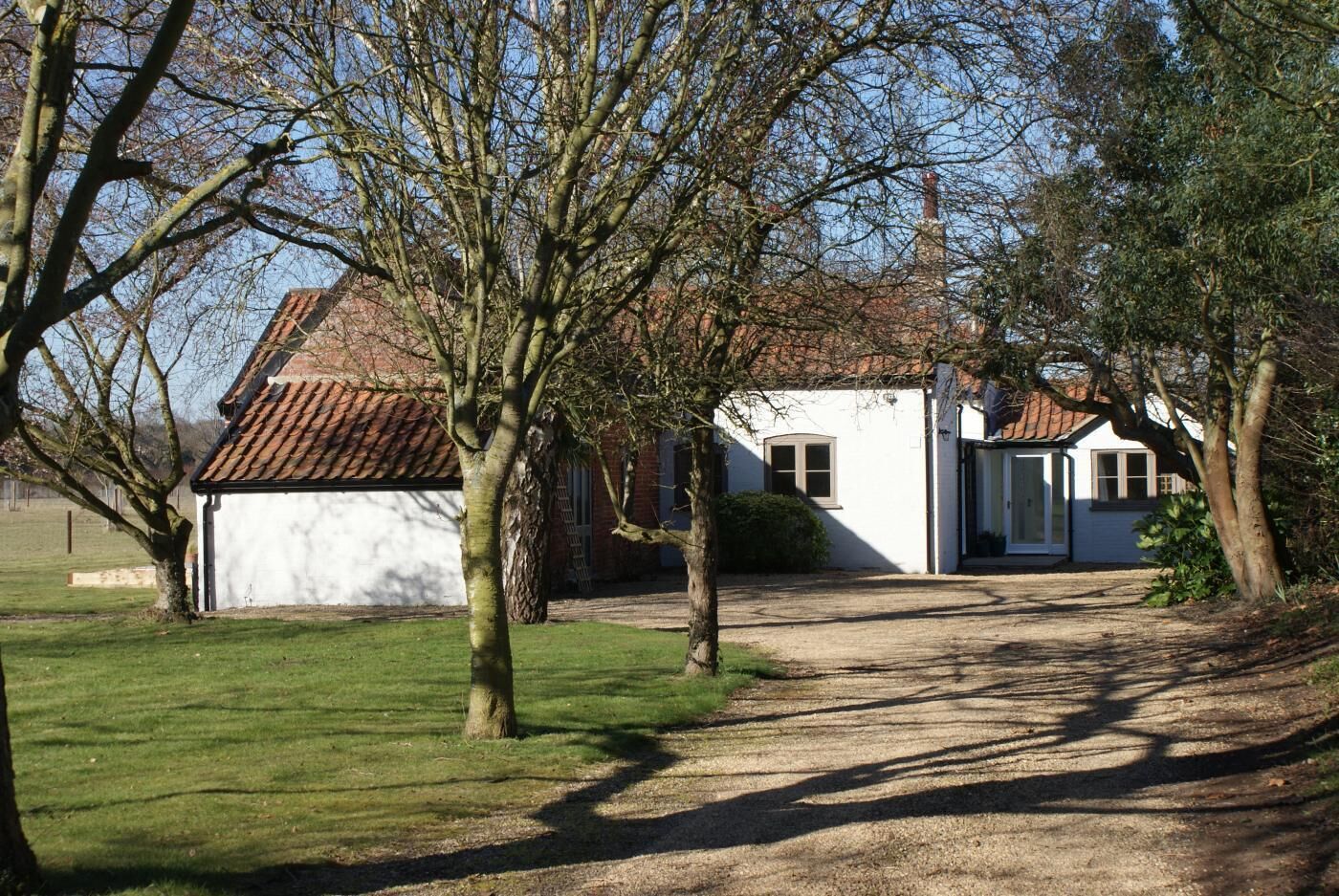 Un bâtiment blanc avec un toit recouvert de tuiles rouges, un porche et une allée gravillonnée.