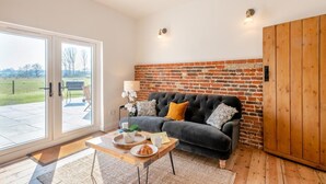 A cozy living room with a black sofa, wooden coffee table, and a brick wall. - 5 Bed in Postwick (oc-w30947) (Postwick)