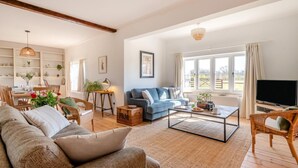 A spacious living room with a sofa, coffee table, and a television. There are wicker chairs, a dining table with chairs, and a bookshelf. - 5 Bed in Postwick (oc-w30947) (Postwick)