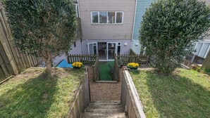 Um imóvel residencial com escadas de madeira levando a uma porta principal, cercado por uma cerca de madeira e duas árvores.