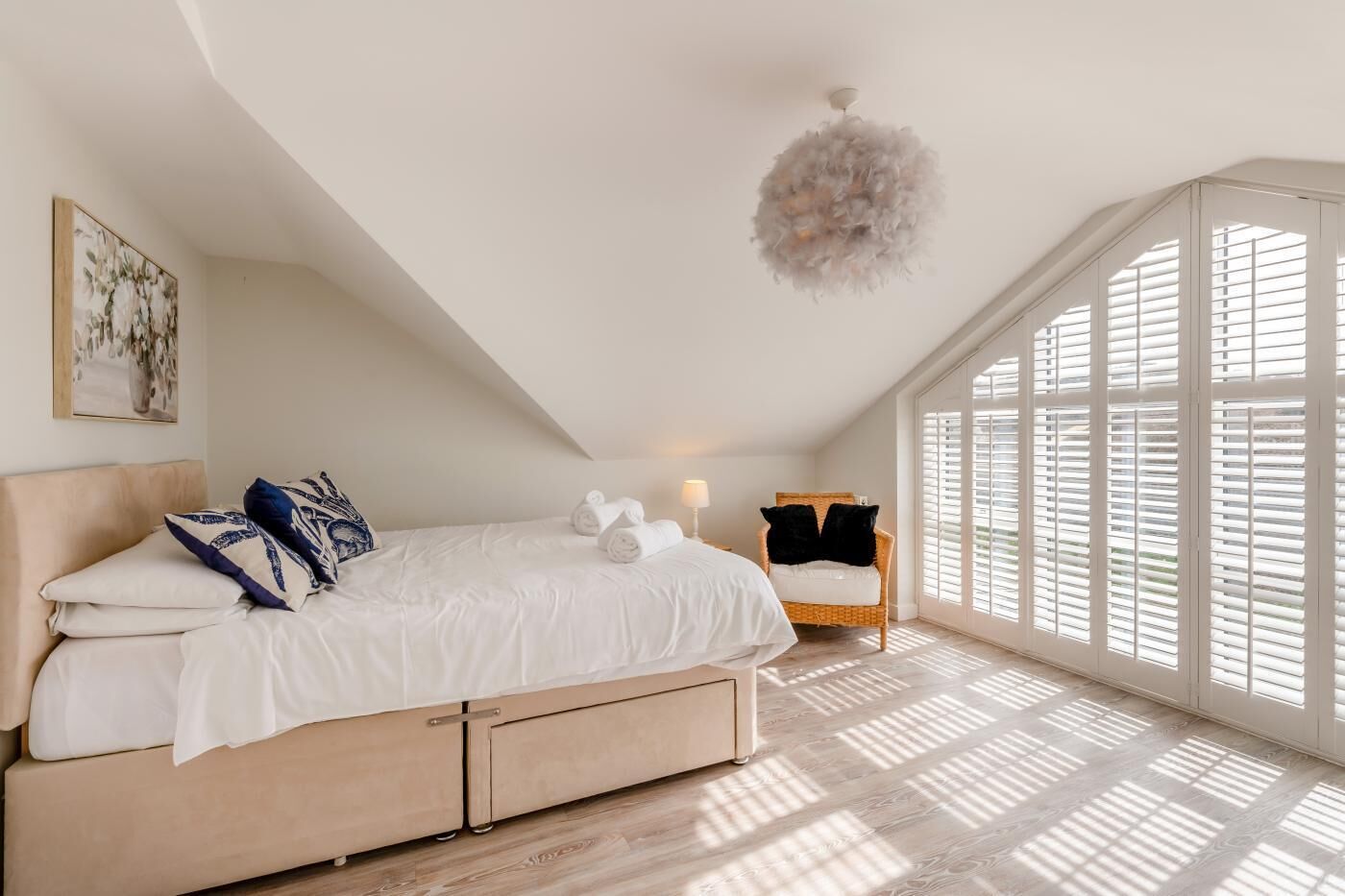 A bedroom with a bed, a chair, a hanging light fixture, and large windows with blinds.