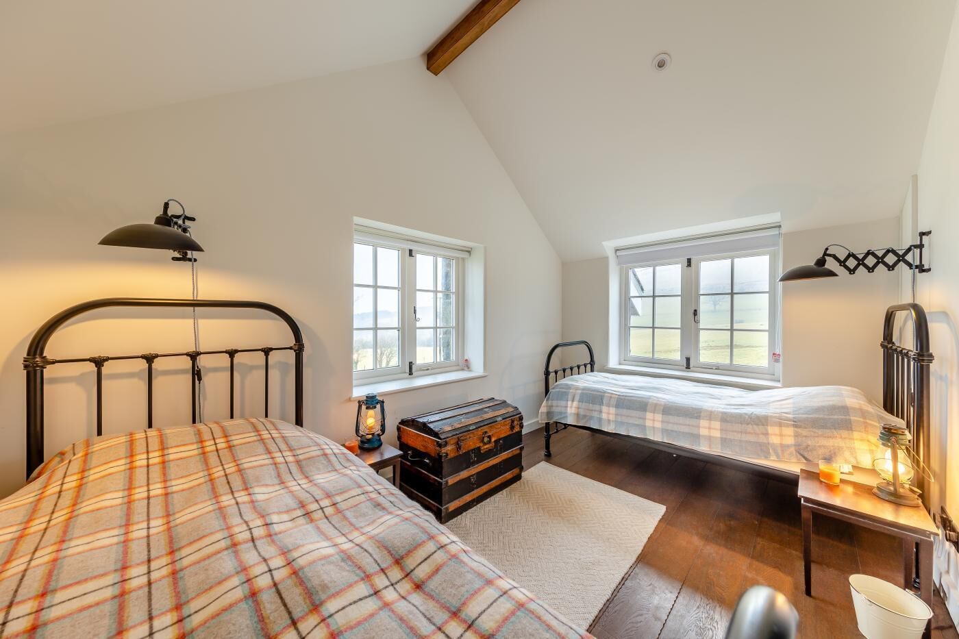 A bedroom with two beds, a wooden chest, and a desk with a lamp.