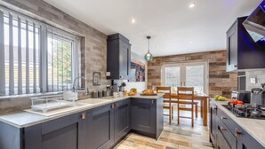 A modern kitchen with dark cabinetry, a large island, and a dining area with wooden chairs.