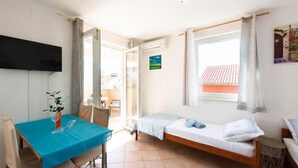 Una habitación pequeña y luminosa con cama, mesa y televisor.