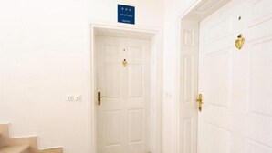 Un pasillo con puertas blancas, un cartel sobre la puerta de la izquierda y una escalera a la izquierda.