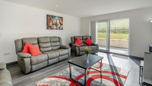 A modern living room with a grey sofa and armchair, a glass door leading to a balcony, and a painting on the wall. - 3 Bed in Cockermouth (oc-o31515) (Setmurthy)