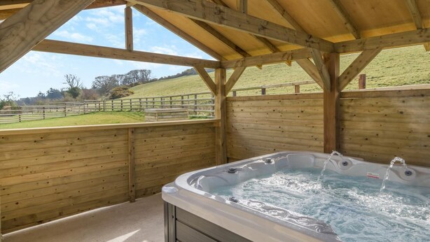 A wooden cabin with a hot tub under a sloped roof, overlooking a grassy field. - 3 Bed in Cockermouth (oc-o31515) (Setmurthy)